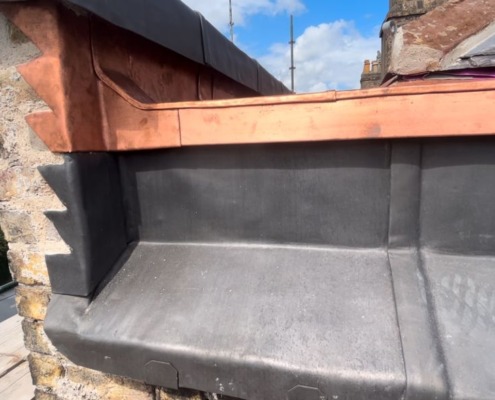 Lined parapet gutter with copper flashing beside a slate roof